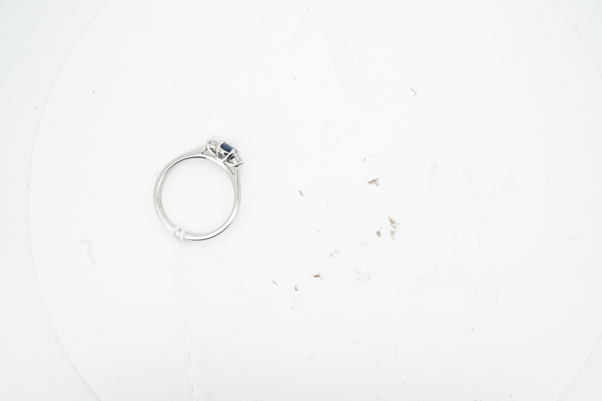 A sapphire and diamond three-stone ring, claw-set with an oval sapphire weighing approximately 0.35 carats, between shoulders set with brilliant-cut diamonds totalling approximately 0.12 carats, mounted in 9ct white gold